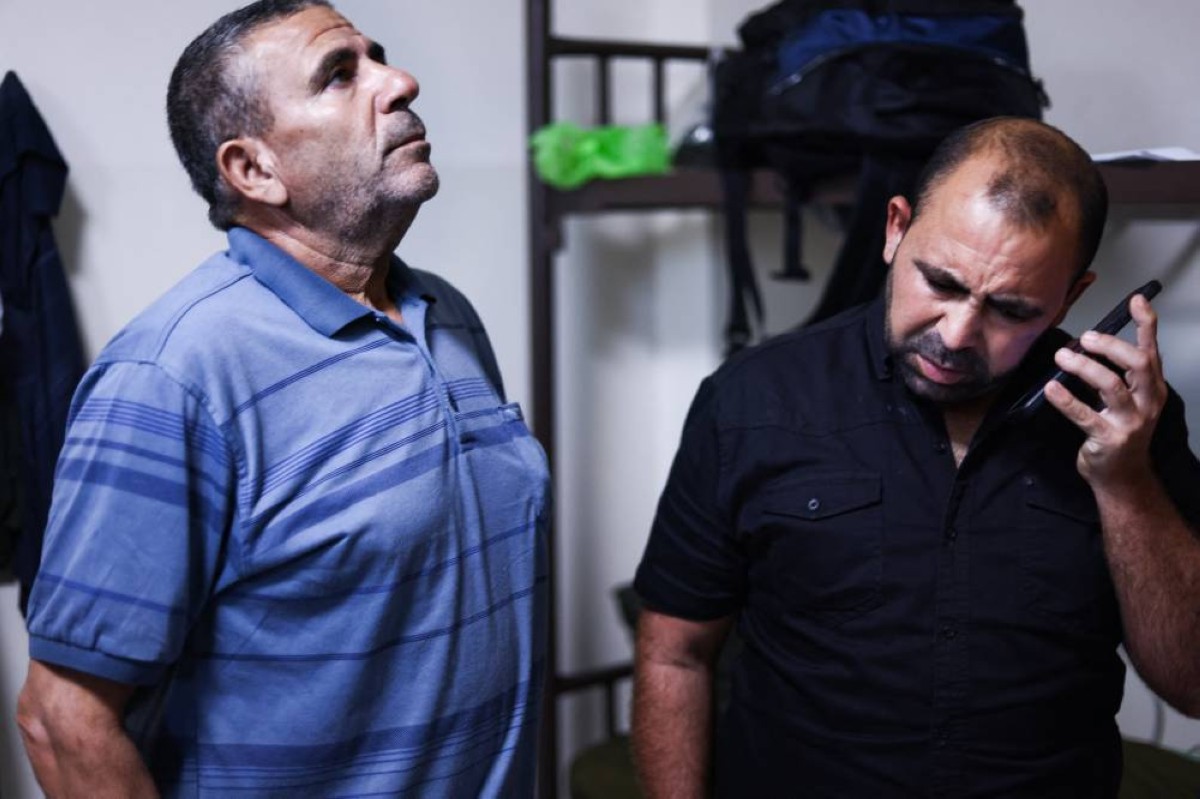 Wissam Mqout (right), a Palestinian worker from the Gaza Strip who had work permit in the Zionist entity, talks on a mobile phone next to his father Ismail.