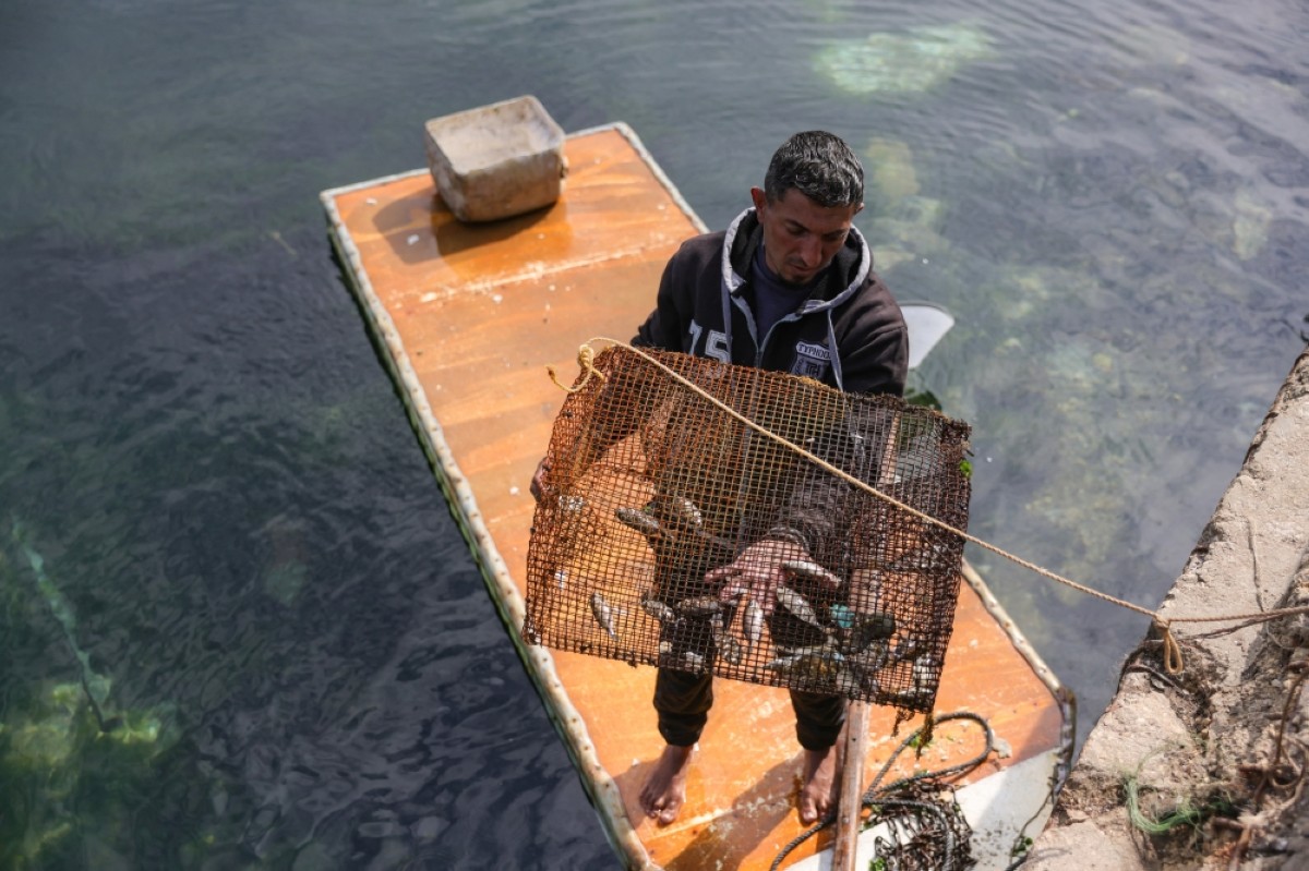 A Palestinian man shows his catch as he stands on the door of a refrigerator that he uses as a makeshift rowing boat, at the port of Gaza City. 