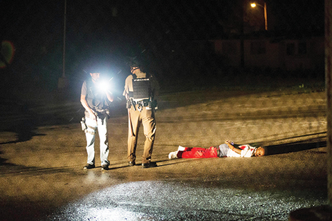 FERGUSON, MO - AUGUST 09: Police stand over a man with gunshot wounds lying in a parking lot after a shoot out with police along West Florissant Street during a demonstration to mark the one-year anniversary of the shooting of Michael Brown on August 9, 2015 in Ferguson, Missouri. The shooter is listed in critical condition in an area hospital. Michael Brown's death sparked months of sometimes violent protests in Ferguson and drew nationwide focus on police treatment of black offenders.   Scott Olson/Getty Images/AFPn== FOR NEWSPAPERS, INTERNET, TELCOS &amp; TELEVISION USE ONLY ==