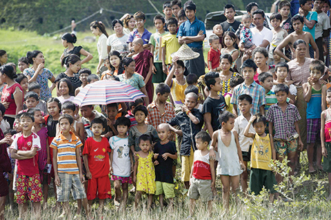 Flood-affected residents gather as they look at a military helicopter (not in picture) delivering food aid at Mrauk U in Myanmar's Rakhine state on August 5, 2015. Tens of thousands of people huddled August 5 in monasteries and other makeshift evacuation centres in remote areas of Myanmar cut off by deadly floods, as rescuers struggled to deliver desperately needed aid. AFP PHOTO / Ye Aung THU