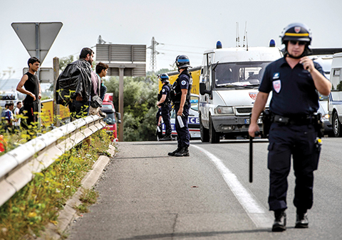 French riot police stand on a road to prevent migrants  from reaching the road leading to the ferry port in Calais, northern France, on August 5,2015. The European Commission offered to help France and Britain deal with the migrant crisis at the Channel Tunnel, as police on both sides braced for new attempts at the crossing. A police source said on August 5 some 350 migrants attempted to enter overnight on to the Channel Tunnel site near Calais. AFP PHOTO / PHILIPPE HUGUEN