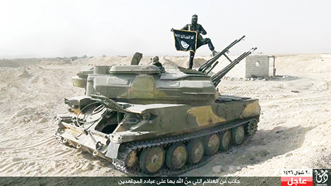 In this picture released on Wednesday, Aug. 5, 2015 by the Rased News Network a Facebook page affiliated with Islamic State militants, an Islamic State militant holds the group's flag as he stands on a tank they captured from Syrian government forces, in the town of Qaryatain southwest of Palmyra, central Syria. The Islamic State group on Thursday seized a key town in central Syria following heavy clashes with President Bashar Assad's forces, in the militants' biggest advance since capturing the historic town of Palmyra in May, Syrian activists said. (Rased News Network a Facebook page affiliated with Islamic State militants via AP)