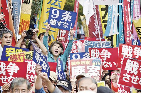 TOPSHOTSnDemonstrators hold placards to protest against Prime Minister Shinzo Abe's controversial security bills in front of the National Diet in Tokyo on September 18, 2015.  Japan was expected to pass security bills on September 18 that would allow troops to fight on foreign soil for the first time since World War II, despite fierce criticism it will fundamentally alter the character of the pacifist nation.   AFP PHOTO / KAZUHIRO NOGI