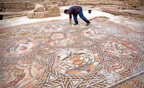 A worker of the Israel Antiquities Authority cleans a 1,700-year-old mosaic, which served as pavement for the courtyard in a villa during the Roman and Byzantine periods, as it is presented to the public and the press for the first time yesterday, in the Israeli central city of Lod. — AFP photos