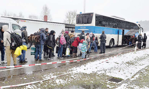 ants queue during a snow shower to board a bus after crossing the border between Austria and Germany in Wegscheid near Passau, Germany, yesterday. — AP