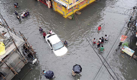 CHENNAI: Indian residents attempt to push a vehicle through floodwaters as others wade past in Chennai yesterday. — AFP