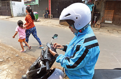 JAKARTA: A female motorcycle taxi driver checking for an order on her smartphone in Jakarta. — AFP