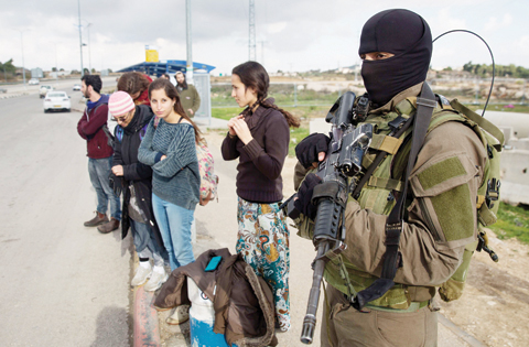 GUSH ETZION: An Israeli soldier from the elite infantry unit stands guard as Israeli settlers stand at a bus station at the Gush Etzion junction in the Israeli occupied on the main road between Jerusalem and Hebron on December 2, 2015. — AFP