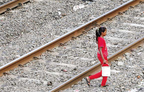 MUMBAI: An Indian girl holds a can filled with water and walks past railway tracks to defecate in the open in Mumbai, India. — AP
