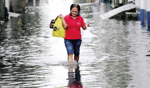 MANILA: A woman walks through floodwaters in suburban Manila yesterday. — AFP