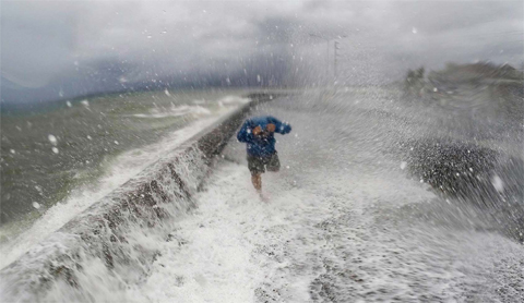 ALBAY PROVINCE: A resident walks past big waves spilling over a wall onto a coastal road in the city of Legaspi.—AFP