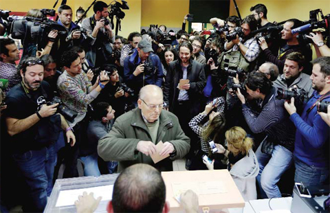 Pablo Iglesias, (center right) leader of Podemos party, waits his turn to cast his vote for the national elections. — AP