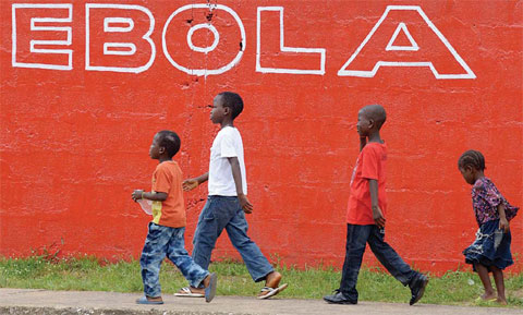 MONROVIA: This file photo taken on August 31, 2014 showing children walk past a slogan painted on a wall reading “Ebola”. —AFP