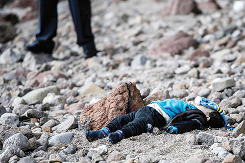 EDITORS NOTE: Graphic content / TOPSHOT - A man stands by the body of a migrant child washed up on a beach in Canakkale's Bademli district on January 30, 2016 after at least 33 migrants drowned when their boat sank in the Aegean Sea while trying to cross from Turkey to Greece, Turkey's state-run Anatolia news agency reported.  The migrants, who included those from Myanmar, Afghanistan and Syria, set sail from the Canakkale province to reach the nearby Greek island of Lesbos, Anatolia said.  / AFP / OZAN KOSE