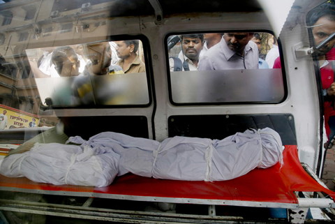 People look at the bodies of two among the victims fatally stabbed by a man as they are kept inside an ambulance outside a hospital in Thane, outskirts of Mumbai