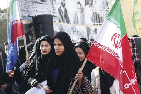 TEHRAN: Schoolgirls hold national flag in front of a giant board as Iranians mark the start of 10 days of celebrations for the 37th anniversary of the Islamic revolution yesterday at the Behesht-e Zahra (Zahra’s Paradise) cemetery in southern Tehran. — AFP