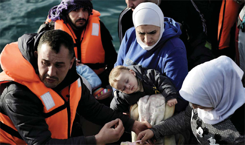 MYTILENE: A woman carries a sleeping child as refugees and migrants disembark a rubber boat upon arrival at the northern island of Lesbos after crossing the Aegean sea from Turkey, in Mytilene, yesterday.—AFP