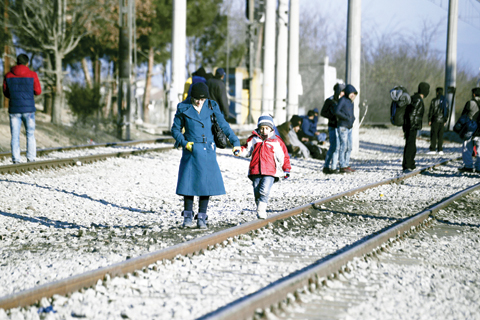 A woman with her child walk alongside railway tracks as refugees wait at a refugee camp to be allowed to continue their journey to Macedonia, near the northern Greek village of Idomeni yesterday. — AP