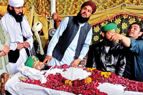 Relatives and supporters stand around the body of Mumtaz Qadri, the convicted killer of a former governor, during funeral ceremonies at his home yesterday. - AP 