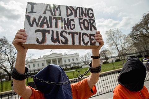 A man dressed as a detainee holds a sign calling attention to the detainees at Guantanamo Bay during a demonstration outside the White House in Washington, Friday, March 11, 2016. A coalition of activists continue to call on the Obama administration to close Guantanamo Bay detention center and end indefinite detention. (AP Photo/Andrew Harnik)