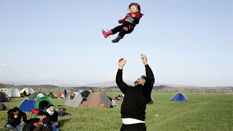 MACEDONIA BORDER: In this file photo, a Syrian man plays with his one-year-old child as refugees and migrants wait to be allowed to cross the border to Macedonia in the northern Greek border station of Idomeni. — AP