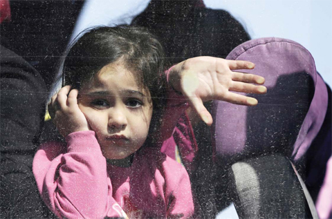 ATHENS: A girl looks out of a bus window after her arrival by ferry with hundreds other migrants and refugees from the northeastern Greek island of Lesbos to the port of Elefsina, west of Athens, yesterday. — AP