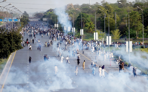 RAWALPINDI: Supporters of executed Islamist Mumtaz Qadri retreat from smoke after tear gas shelling by authorities during an anti-government protest yesterday. — AFP