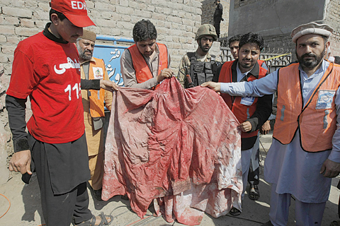 SHABQADA: Pakistani volunteers show a blood-soaked burqa of a woman who was killed in an a suicide bombing in the town of Shabqadar, Charsadda district, Pakistan, yesterday. —AP