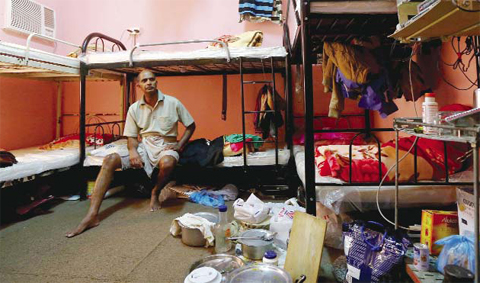 DOHA: This file photo shows Kupttamon, an Indian laborer working in Qatar, sitting in his tiny over-crowded room at a private camp housing foreign workers in Doha. — AFP