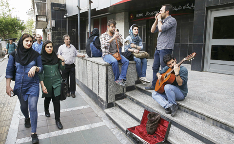 TEHRAN: Iranian women walk past youths playing music on the sidewalk in downtown Tehran on Tuesday. - AP 