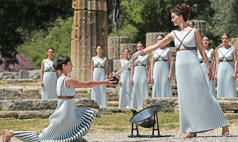 Actress Katerina Lechou (right) acting the high priestess passes the Olympic flame at the Temple of Hera yesterday during the lighting ceremony of the Olympic flame in ancient Olympia, the sanctuary where the Olympic Games were born in 776 BC. — AFP