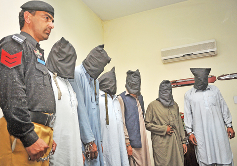 PESHAWAR: A Pakistani policeman stands guard alongside suspects who allegedly killed Sikh politician Sardar Soran Singh during a press conference after their arrest in Peshawar. — AFP