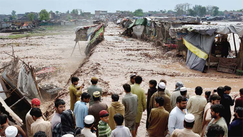 PESHAWAR: Pakistani vendors and residents gather beside flood waters rushing through a market area yesterday. — AFP