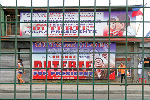 In this Wednesday, May 11, 2016 photo, residents walk past giant tarpaulins of presumptive President-elect Rodrigo Duterte at his hometown in Davao city, southern Philippines. A bold campaign promise to eradicate crimes and corruption within six months and his iron-fist approach to law and order helped catapult the longtime mayor to the presidency, but Duterte's anti-crime reputation is also a political baggage that would haunt him now as he comes under the spotlight. (AP Photo/Bullit Marquez)