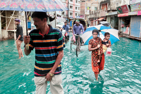 DHAKA, BANGLADESH: Bangladeshi people walk through a waterlogged street after heavy rainfall on Saturday. — AP
