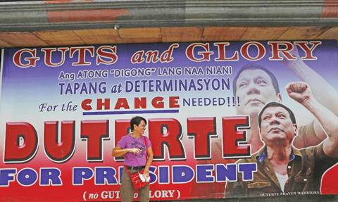 DAVAO CITY: A resident stays in the shade behind a campaign billboard of leading presidential candidate Mayor Rodrigo Duterte along a boulevard at his hometown. — AP