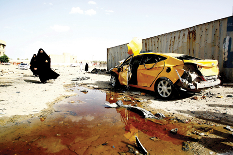 SAMAWAH, Iraq: Iraqi women walk past a damaged car following a twin suicide bombing attack claimed by the Islamic State (IS) group in this southern Iraqi city yesterday. — AFP