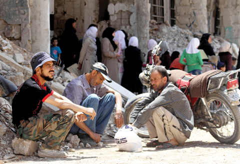 DARAYA, Syria: Syrian men sit next to a damaged building in this town southwest of Damascus yesterday. — AFP