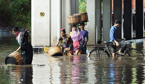 MUMBAI: Indian pedestrians and a cyclist wade through a flooded street after heavy monsoon rain showers in Mumbai. - AFP 