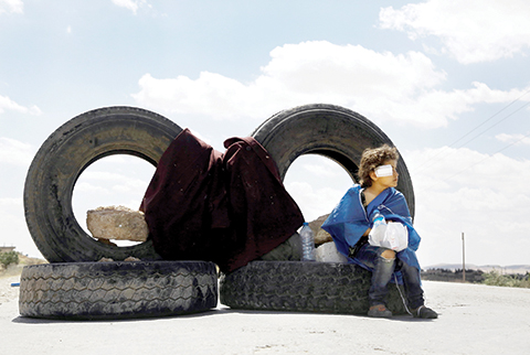 A young wounded girl sits on a tyre as she holds her medicines at a road block set up by fighters from the Syrian Democratic Forces (SDF) on June 10, 2016 on the outskirts of the northern Syrian town of Manbij, held by the Islamic State (IS) group, as they encircled the town cutting off the jihadists main supply route between Syria and Turkey. IS lost control of a vital supply artery when the troops completely surrounded the town of Manbij, at the heart of the last stretch of territory along Turkey's border still under the jihadists' control.nn / AFP / DELIL SOULEIMAN