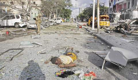 MOGADISHU: A member of security forces guards the scene near an unidentified dead body after a bomb attack on Ambassador Hotel in Mogadishu, Somalia yesterday. — AP