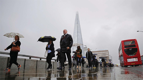 LONDON: Commuters heading into the City of London walk in the rain across London Bridge in front of the Shard skyscraper in central London yesterday. —AFP