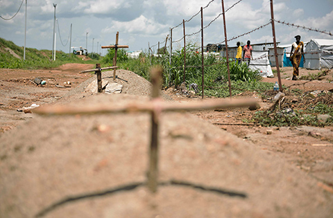 People walk on the other side of barbed wire where makeshift graves were placed at the United Nations Mission in the Republic of South Sudan (UNMISS), the UN House for internally displaced persons in the Jebel area in Juba on July 22, 2016.  About 10,000 people have been displaced since the fighting began in Juba on the 8th of July 2016. According to a camp manager 137 people suffered from gunshot wounds and were being treated in the camp clinics, but some had succumbed to their injuries so they had been buried. Juba was rocked by days of heavy fighting in early July between government forces and fighters loyal to current Vice President Riek Machar which erupted as he was meeting President Salva Kiir in the presidential palace. More than 300 people were killed and tens of thousands of people fled, escalating fears of a return to the brutal civil war that erupted just over two years after independence in 2011. The latest violence in the capital echoed the fighting that first triggered the civil war in December 2013, when Kiir accused Machar of plotting a coup. / AFP / CHARLES ATIKI LOMODONG