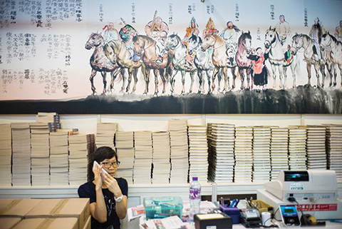 A vendor uses her phone in her stall at the annual book fair in Hong Kong on July 20, 2016. Hong Kong's feisty publishing industry vowed to take on China by selling books critical of Beijing, despite the disappearances of five city booksellers, as a major annual book fair began on July 20. / AFP / Anthony WALLACE
