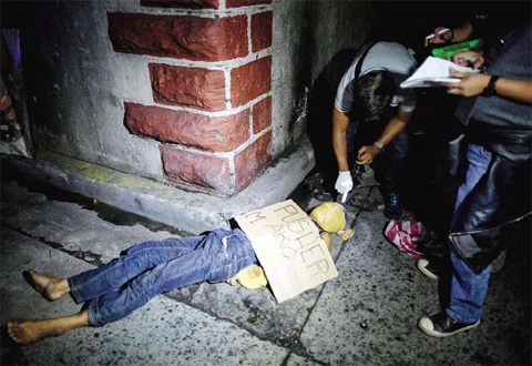 MANILA: In this picture taken on July 8, 2016, police officers investigate the dead body of an alleged drug dealer, his face covered with packing tape and a placard reading “I’m a pusher”, on a street. — AFP