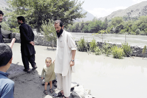 NAGAR, Pakistan: Residents affected by flooding gather on higher ground alongside floodwaters in this village in Chitral yesterday. - AFP 