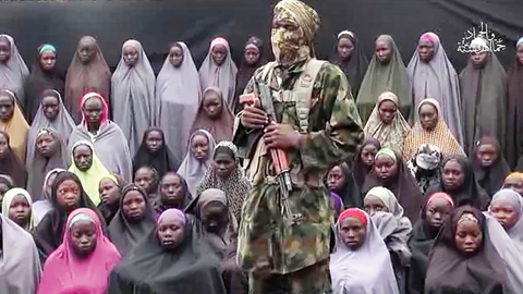 This video grab taken from a video released by Boko Haram yesterday shows what is claimed to be one of the group's fighters at an undisclosed location standing in front of girls allegedly kidnapped from Chibok in April 2014. - AFP  