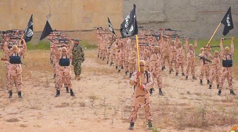 In this file photo released by a militant website, young boys known as the ‘lion cubs’ hold rifles and Islamic State group flags as they exercise at a training camp