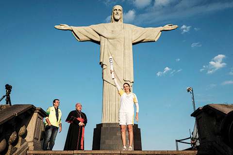 TOPSHOT - Olympic torch bearer Brazilian former volleyball player Maria Isabel Barroso Salgado (R) holds up the torch of Rio 2016 Olympic games with the City Mayor Eduardo Paes (L) and Archbishop of Rio de Janeiro Orani Tempesta in front of the statue of Christo the Redeemer atop Corcovado Hill in Rio de Janeiro on August 5, 2016. The carnival capital of Rio de Janeiro will host a glittering Olympics opening ceremony party, hoping to draw a line under a turbulent seven-year build-up dogged by recession, drugs scandals, crime and infrastructure stumbles. / AFP / YASUYOSHI CHIBA