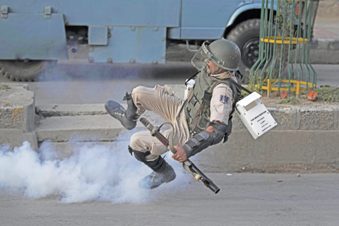 KASHMIR: An Indian paramilitary soldier falls down as he tries to kick back an exploded tear gas shell thrown back at them by Kashmiri Muslim protesters yesterday. — AP